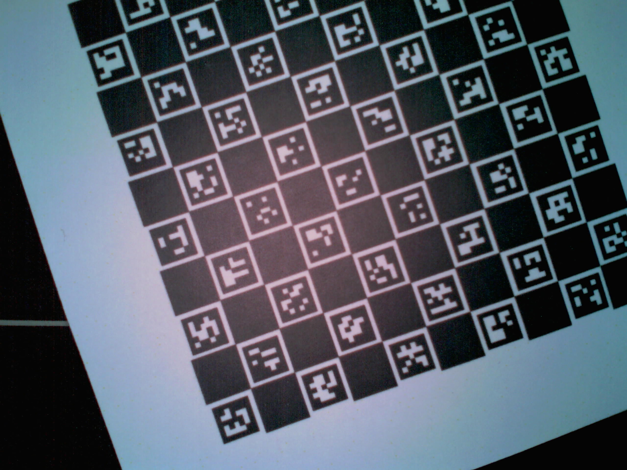 The camera's view of a ChArUco calibration target — a black-and-white chequerboard filled with small ArUco marker patterns, photographed at a slight tilt on the machine bed.